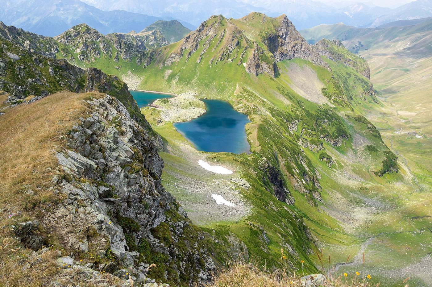 A turquoise glacier lake in a green mountain valley below rocky peaks with a winding shoreline.